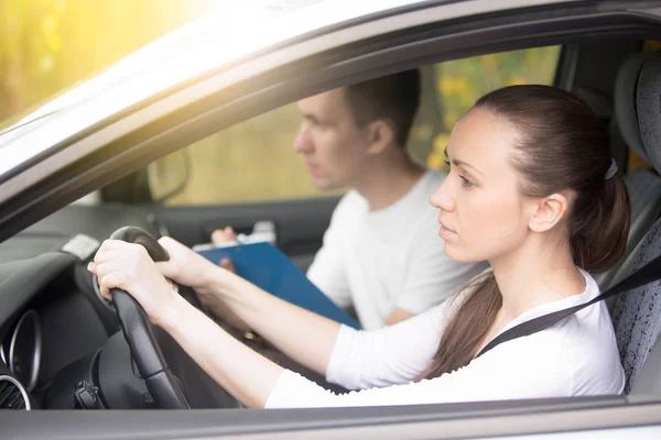 Driving test. Young woman driving a car, man sitting aside — Stock Photo, Image