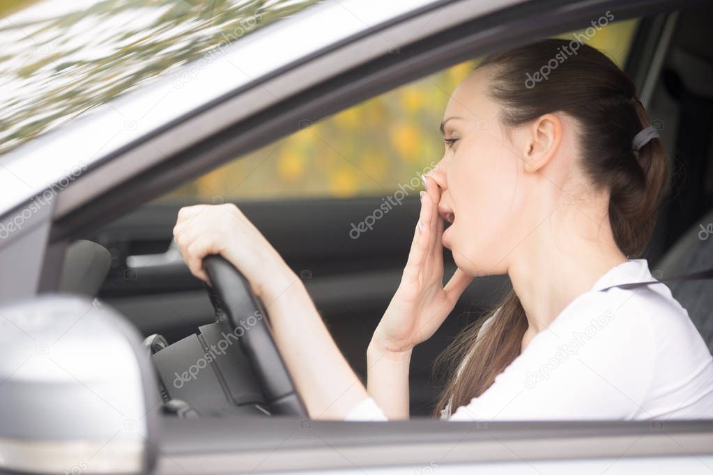 Young woman holding her head at steering wheel