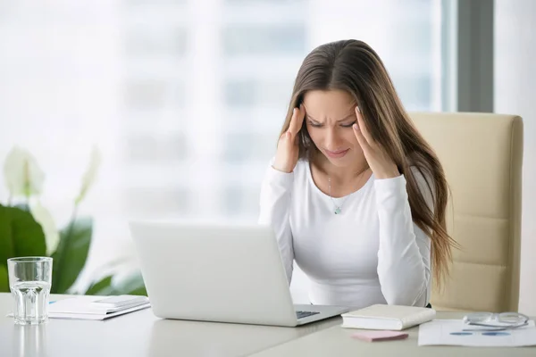 Młoda kobieta, trzymając głowę z bólem w pobliżu laptopa — Zdjęcie stockowe