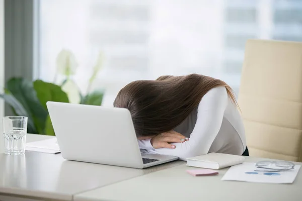Молодая женщина лежит в офисе рядом с ноутбуком — стоковое фото