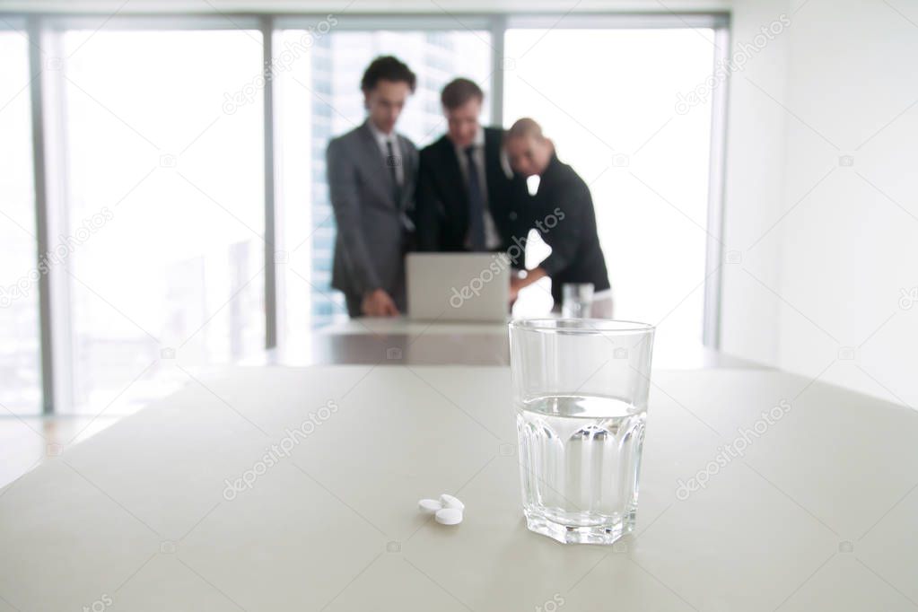 Closeup of a glass of water and pills on an office desk