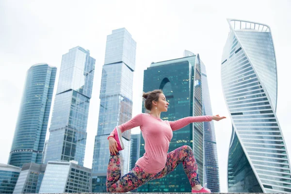 Mladá žena v anjaneyasana pozice na městské pozadí — Stock fotografie