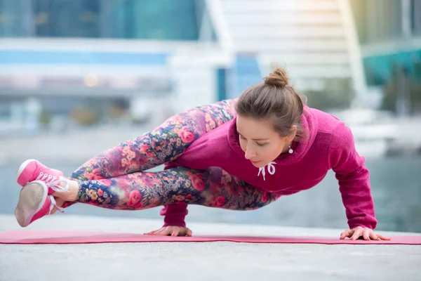 Young woman in Astavakrasana pose against the city and river — Stock Photo, Image