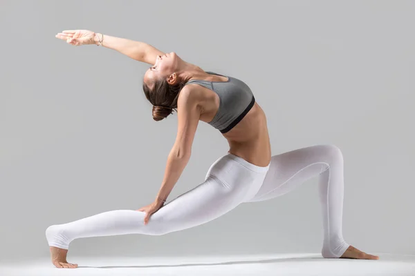 Young woman in anjaneyasana pose, grey studio background