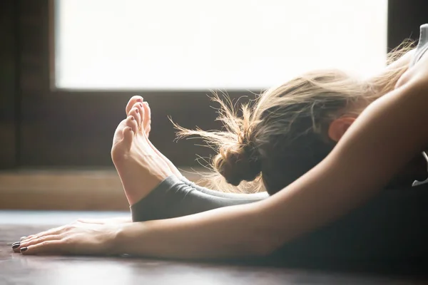 Jonge vrouw in paschimottanasana poseren, home interieur achtergrond, — Stockfoto