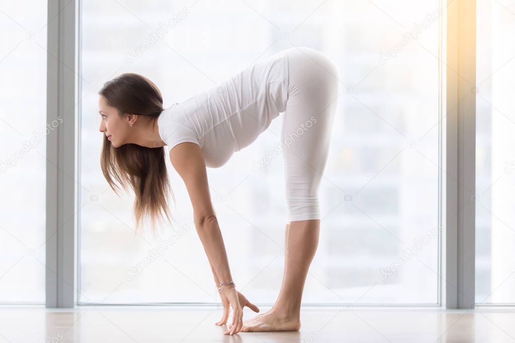 Young attractive woman in Ardha uttanasana pose against floor wi