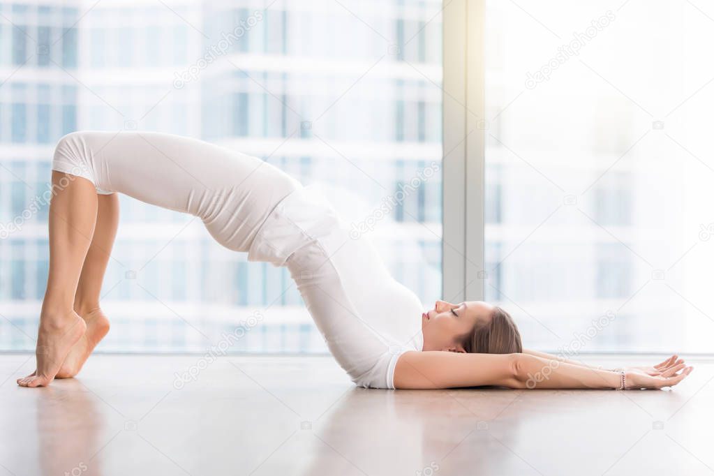 Young attractive woman in Glute Bridge pose against floor window