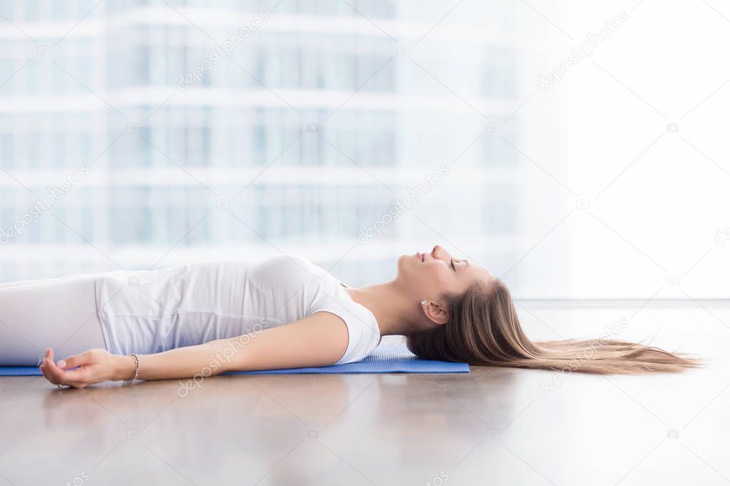 Closeup of young woman in Savasana pose against floor window