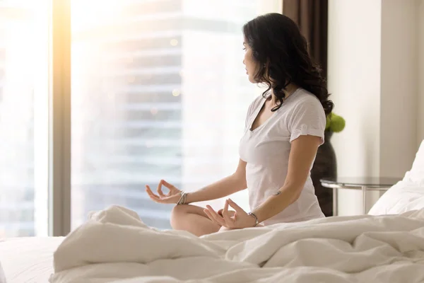 Young woman in Ardha Padmasana pose on the bed, profile — Stock Photo, Image