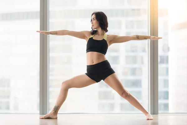 Young attractive woman in Warrior Two pose against floor window — Stock Photo, Image