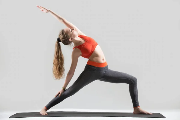 Young attractive woman standing in Reverse Warrior pose, grey st — Stock Photo, Image