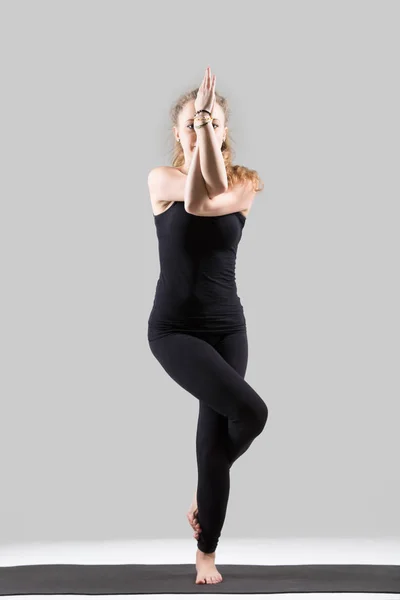 Mujer atractiva joven de pie en la pose Garudasana, estudio gris — Foto de Stock