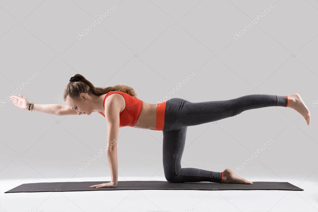 Young attractive woman in Bird dog pose, grey studio background