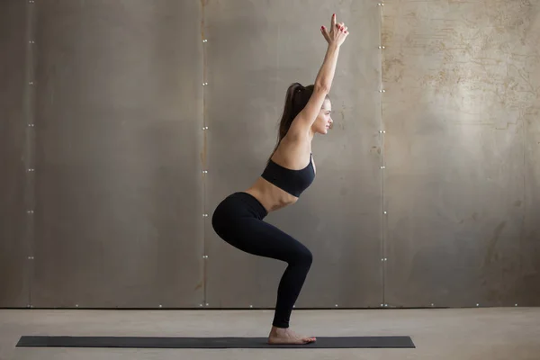 Young attractive woman standing in Utkatasana pose, grey studio — Stock Photo, Image