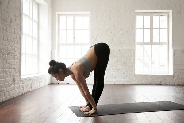 Young attractive woman in Uttanasana pose, white loft studio bac — Stock Photo, Image