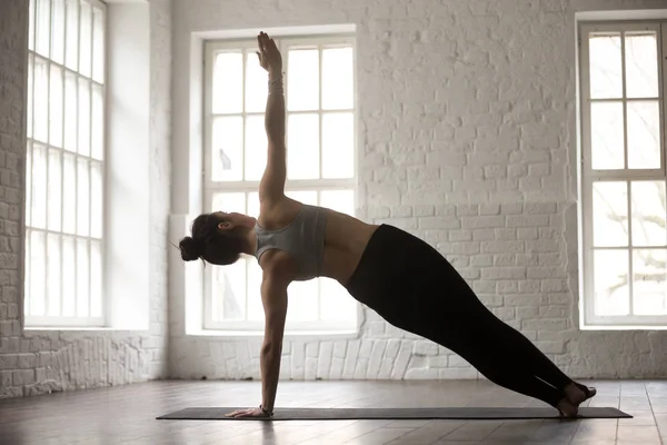 Young woman in Side Plank pose, white studio, rear view