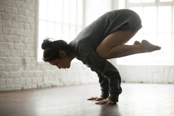 Mujer atractiva joven en la pose Bakasana, respaldo estudio loft blanco — Foto de Stock