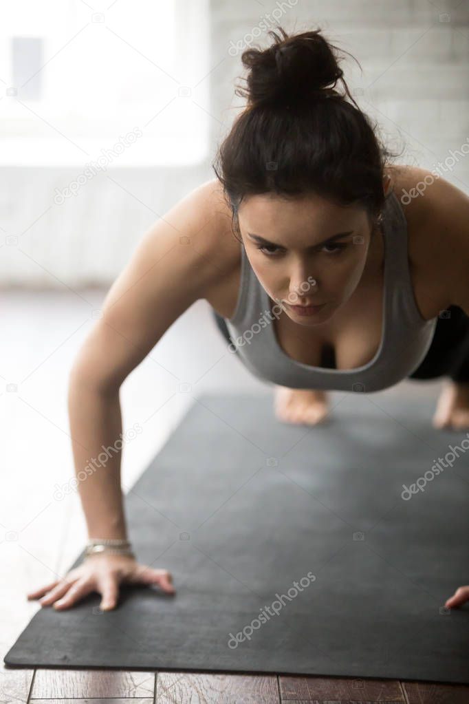Young sporty woman doing press ups exercise, white loft studio