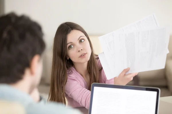 Surprised young woman showing papers to man with questioning loo