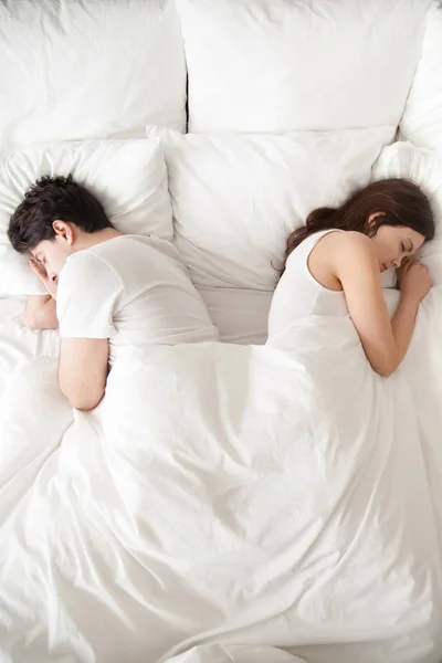 Nuori pari nukkuu erikseen sängyssä, selkä selkää vasten, pystysuora — kuvapankkivalokuva