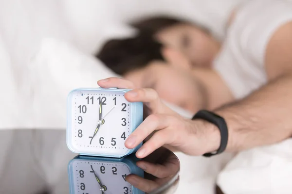 Couple being woken by alarm, man turning off ringing clock — Stock Photo, Image