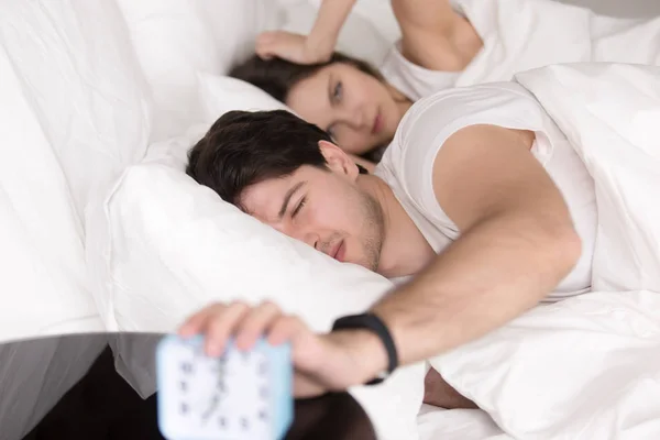 Sleepy angry couple in bed turning off the alarm clock — Stock Photo, Image