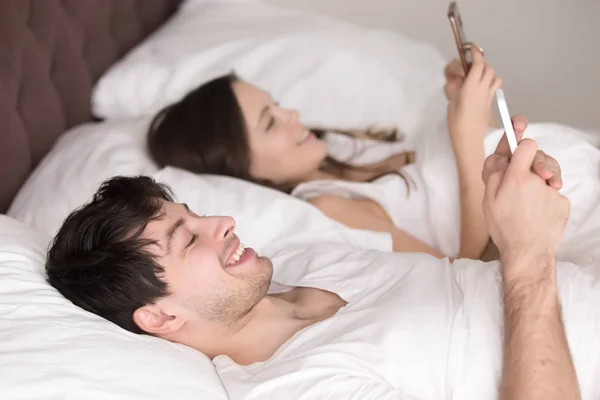 Alegre pareja adolescente en la cama usando teléfonos inteligentes para enviar mes — Foto de Stock