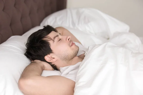 Молодий красивий чоловік відпочиває один в ліжку з закритими очима — стокове фото