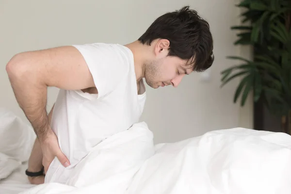 Jonge man zittend op bed thuis raken pijnlijke rug — Stockfoto