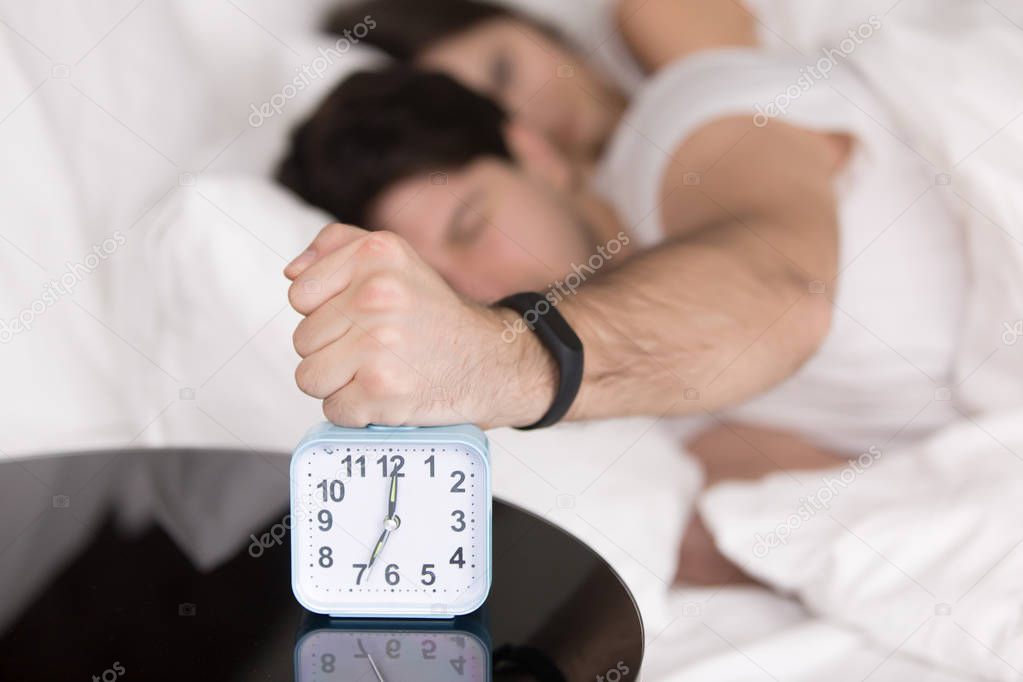 Couple waking up early, guy turning off annoying alarm clock