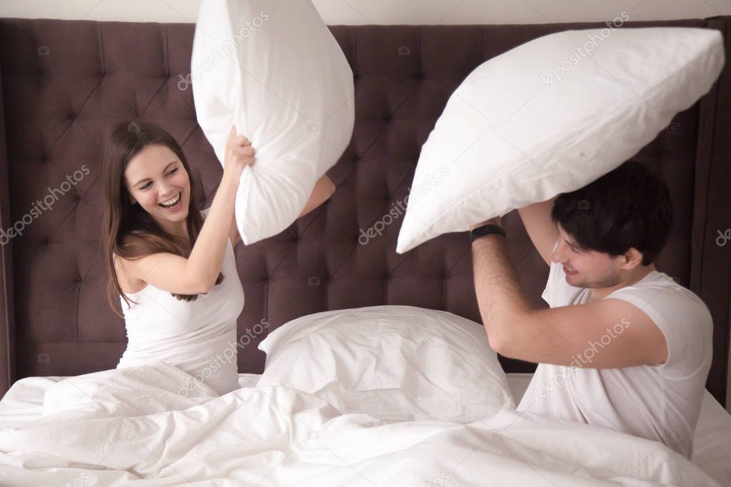 Young happy couple having fun on bed fighting with pillows