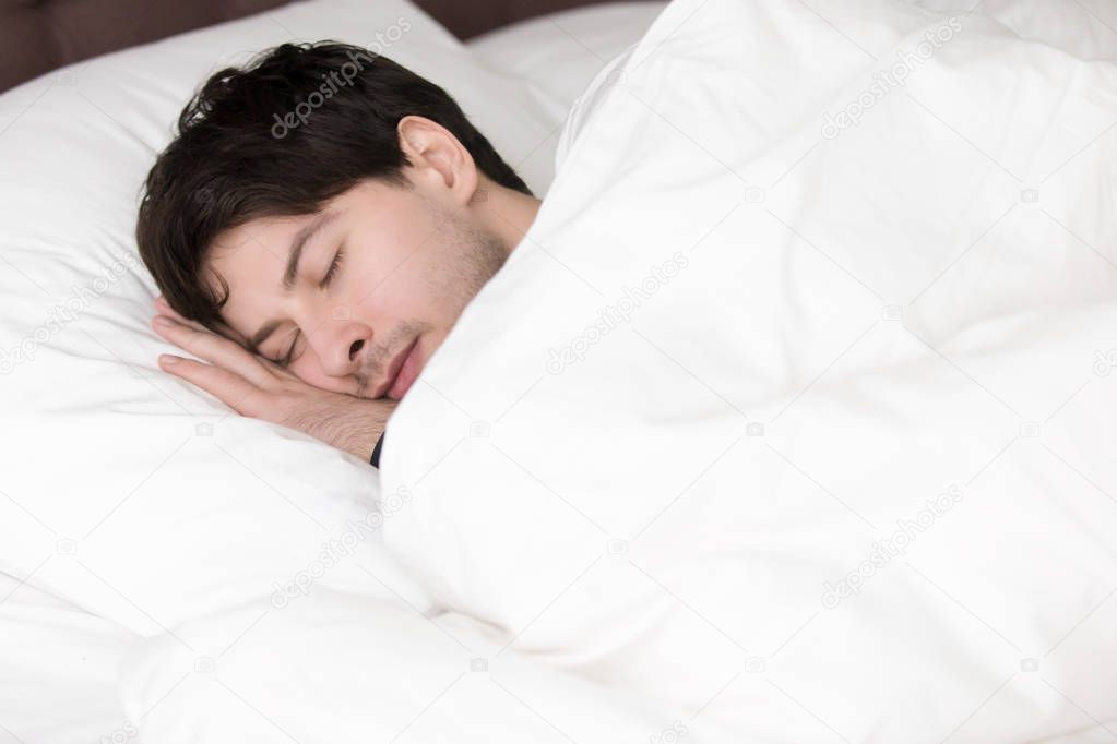 Young handsome man sleeping alone in white bed, soft linen