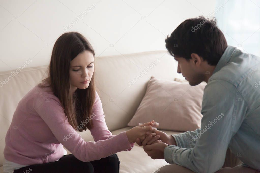 Young man holding hands of upset crying woman, comforting her