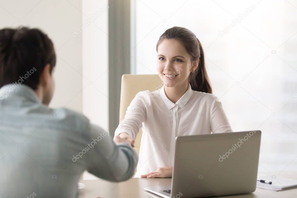 Friendly young businesswoman shaking hands with client, partner