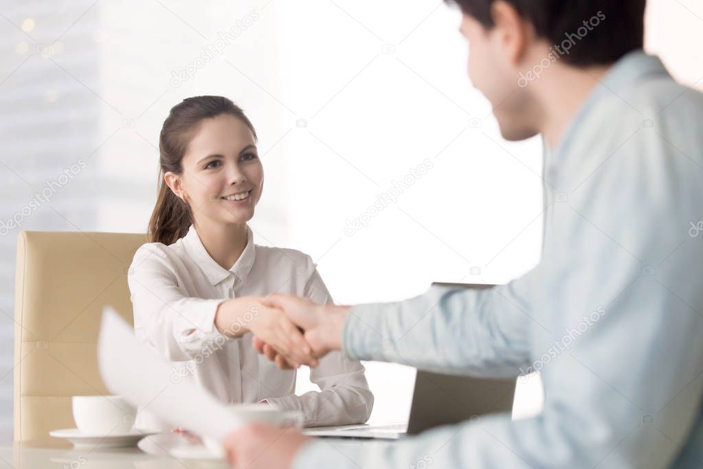 Young businesswoman sitting at office desk handshaking with stan