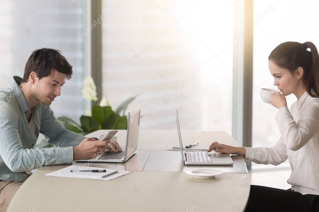 Female and male office workers using laptops having coffee break