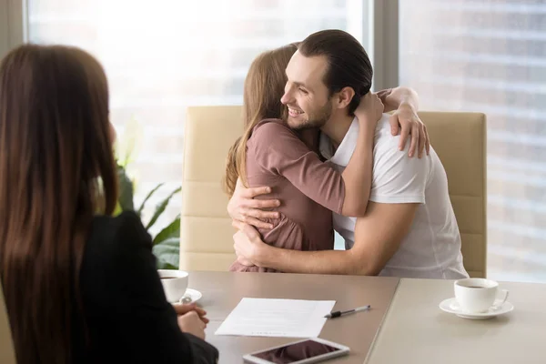 Feliz jovem casal abraçando em reunião com agente imobiliário — Fotografia de Stock