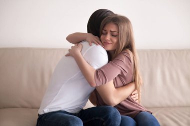 Portrait of young couple hugging tight sitting on couch indoors clipart
