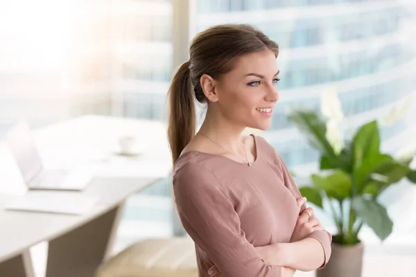 Giovane donna sorridente pensierosa che guarda la finestra, braccia incrociate, ind — Foto Stock