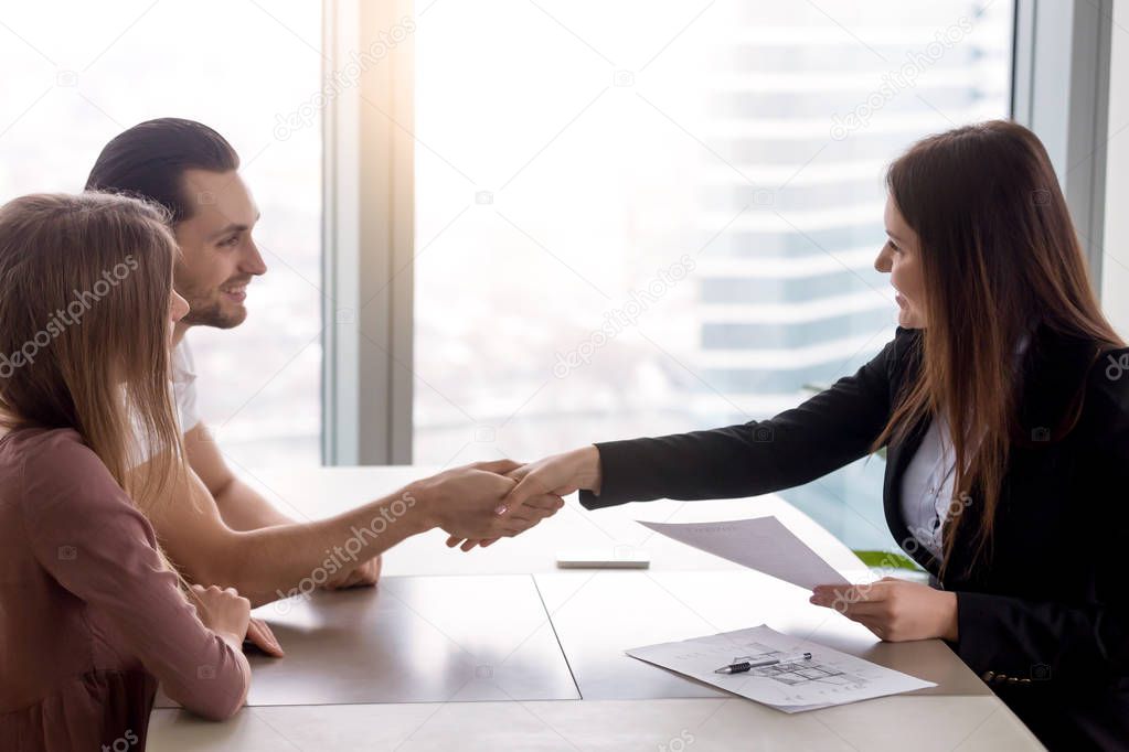 Real estate agent and couple shaking hands office desk