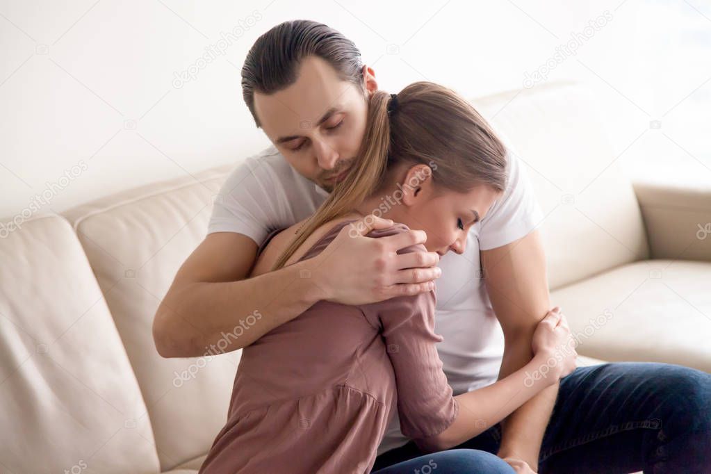 Portrait of young happy couple hugging sitting on couch indoors