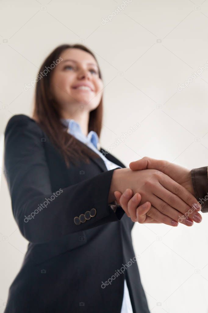 Happy businesswoman wearing suit shaking male hand, focus on han