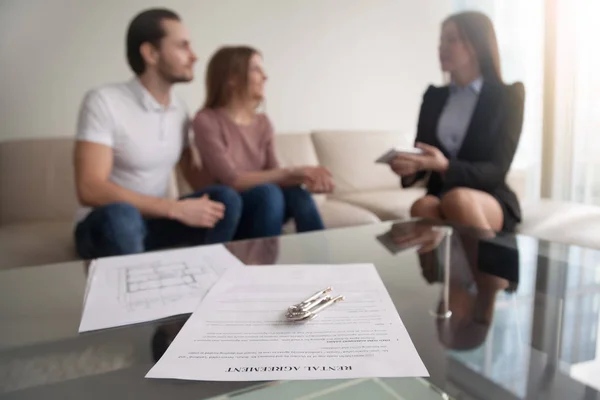 Couple meeting with realtor, focus on rental agreement and keys