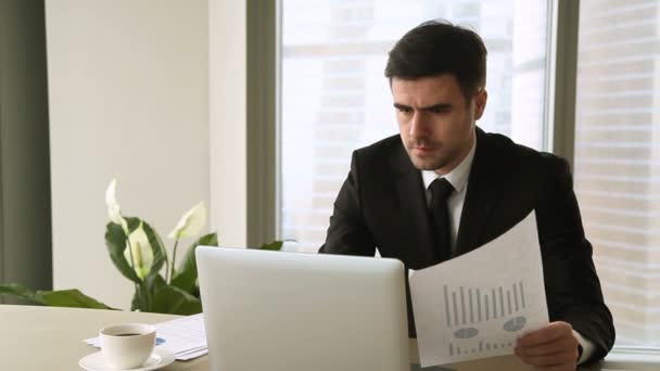 Злой обеспокоенный бизнесмен, работающий на ноутбуке, имеющий проблемы с документами — стоковое видео