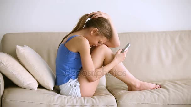 Sad teen girl checking phone and crying sitting on couch — Stock Video