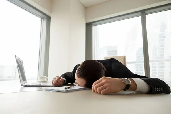 Exhausted businessman lying on his desk in office — Stock Photo, Image