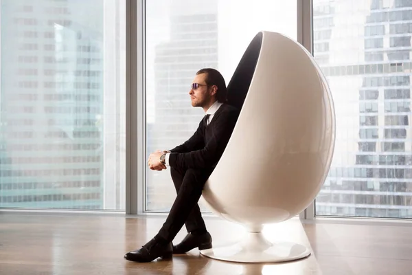 Successful businessman resting in modern egg chair
