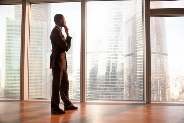 Young african contemplative businessman looking through big wind — Stock Photo, Image