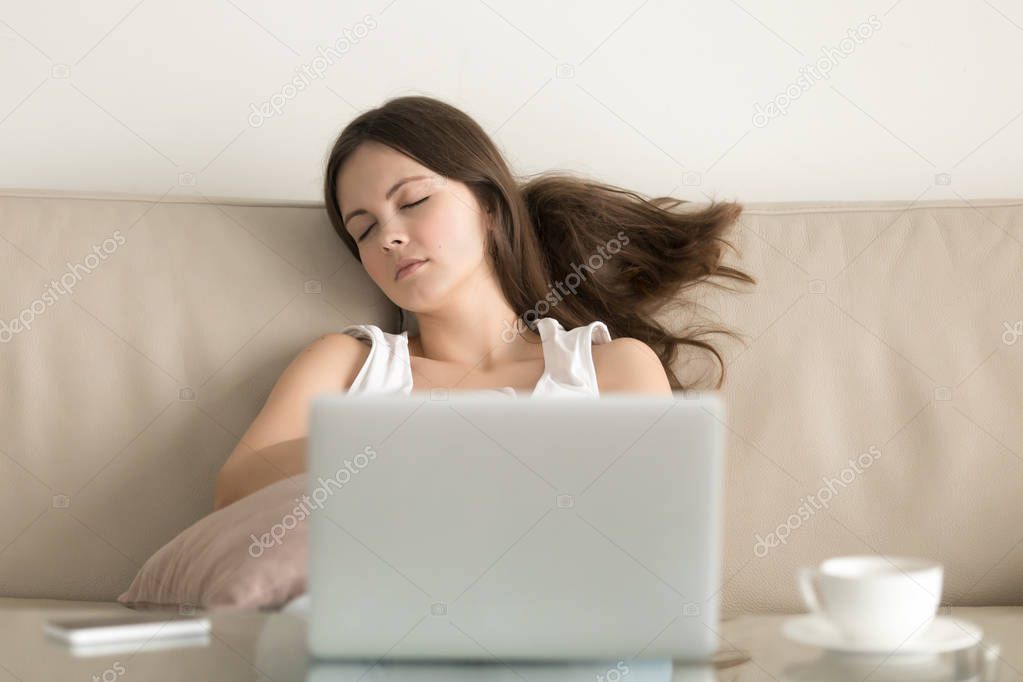Woman falling asleep on sofa in front of laptop