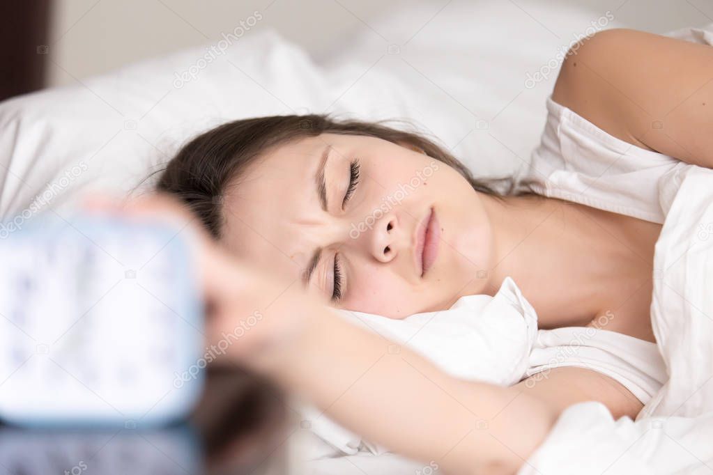 Sleepy young woman turns off signal of alarm clock